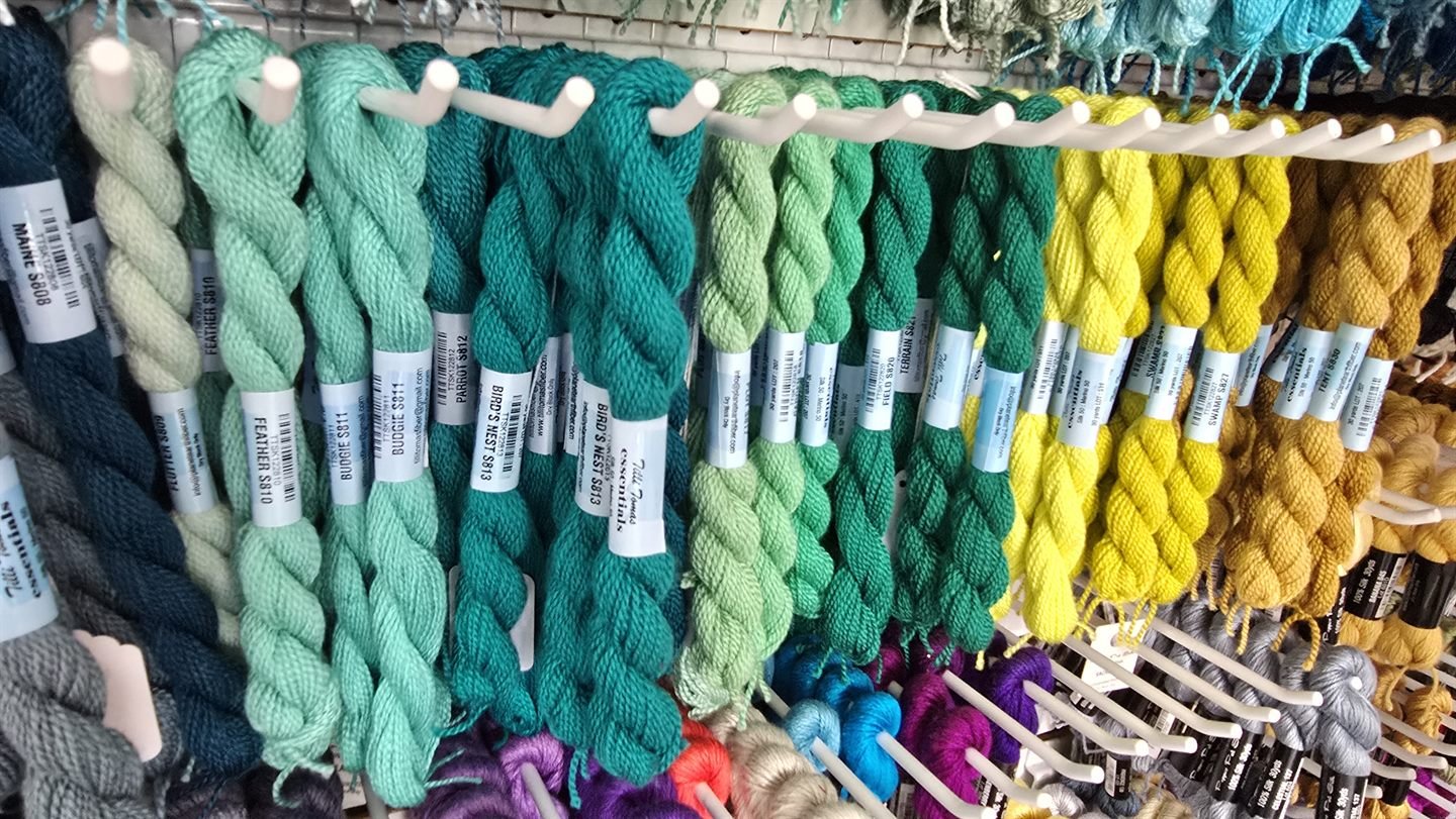 Green and teal thread skeins hanging in a row on a shop wall, with yellow and gold skeins beside them.
